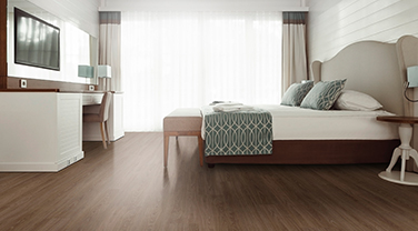 A white bed in front of a window with a white curtain, light shining through