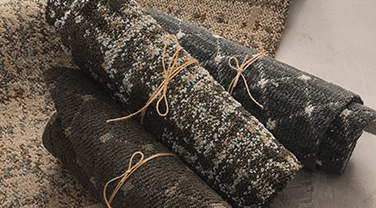 Three rolled bundles of carpet, tied with string, set on a laid out piece of carpet